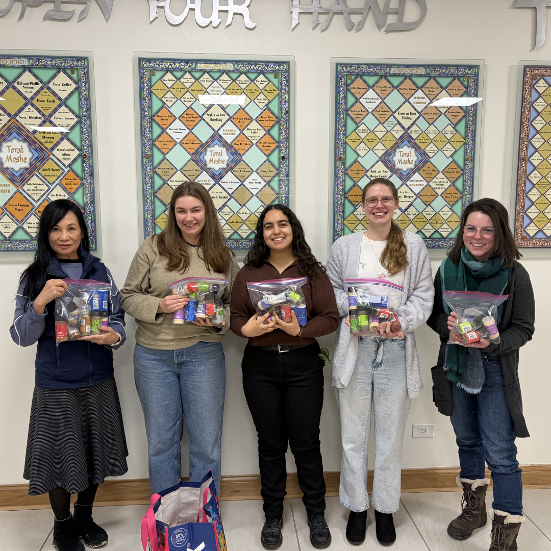 Five volunteers standing together indoors, each holding a clear bag filled with supplies, smiling at the camera